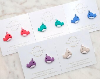 May include: Various pairs of handmade polymer clay narwhal earrings in colours such as red, teal, blue, purple, and beige. Each pair is presented on a white card with the text "Happy Little Clay Co."