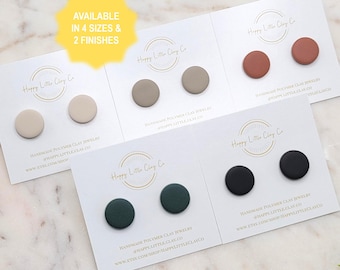May include: Four sets of handmade polymer clay stud earrings in various colors: beige, taupe, terracotta, dark green, and black. Each pair is displayed on a white card with the Happy Little Clay Co. logo. The text "AVAILABLE IN 4 SIZES & 2 FINISHES" is also visible.