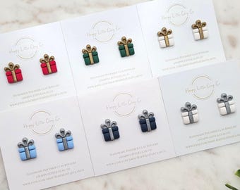 May include: Stud earrings in the shape of gift boxes in various colors, including red, green, white, blue, and black. Each pair is displayed on a white card with the text "Happy Little Clay Co."