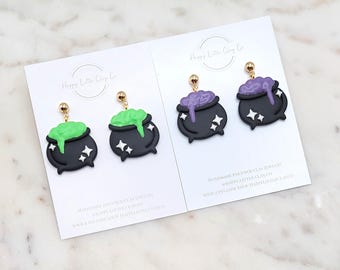 May include: A pair of black cauldron earrings with green and purple bubbling potion. The earrings are made of polymer clay and have gold-colored earring posts. The earrings are displayed on white cards with the Happy Little Clay Co. logo.