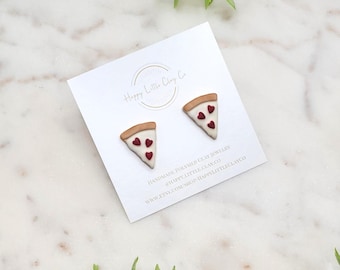 Könnte beinhalten: Ein Paar handgefertigte Ohrringe aus Polymer Clay in Form von Pizzastücken mit roten Herzen als Peperoni. Die Ohrringe befinden sich auf einer weißen Karte mit dem Text "Happy Little Clay Co." und Website-Informationen.