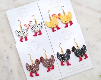 May include: Four pairs of handmade polymer clay chicken earrings. Each chicken has a red comb and boots. The chickens are white with black spots, yellow with white spots, brown with white spots, and black with white spots. Gold-colored earring hooks.