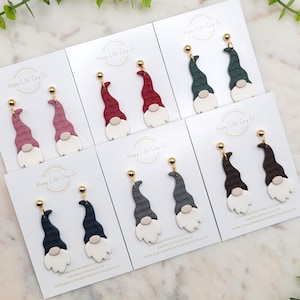 Puede incluir: Surtido de pendientes de arcilla polimérica con forma de gnomo en varios colores, incluyendo rojo, rosa, verde, gris y marrón. Cada pendiente tiene una barba blanca y un gancho dorado.