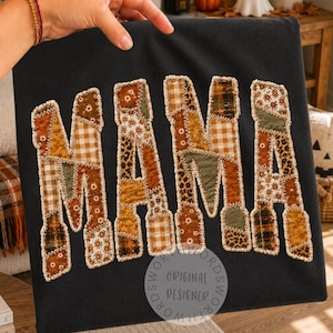 May include: A black t-shirt featuring the word MAMA in large, block letters. Each letter is constructed from a patchwork of various fabric patterns in shades of brown, orange, cream, and green, including gingham, floral, and leopard prints.