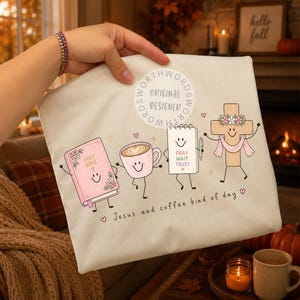 May include: A cream-colored fabric item featuring a graphic of a smiling pink Holy Bible, a pink coffee cup, a white notepad with the text PRAY WAIT TRUST, and a wooden cross with a pink scarf. The text Jesus and coffee kind of day is printed below.