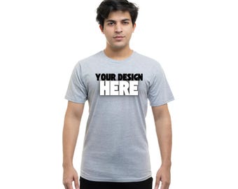 Puede incluir: Una camiseta gris jaspeada de manga corta y cuello redondo. La camiseta tiene el texto "YOUR DESIGN HERE" impreso en la parte delantera en negro y blanco.