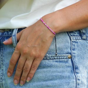 May include: A pink and white beaded bracelet with a black cord and silver bead.