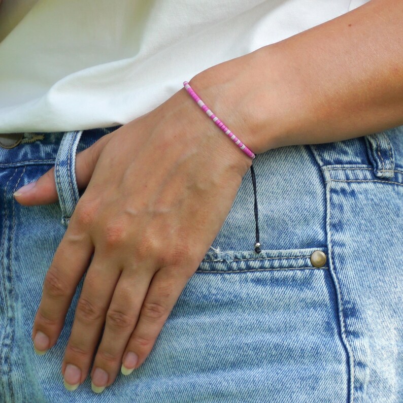 May include: A pink and white beaded bracelet with a black cord and silver bead.
