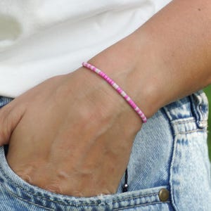 May include: A pink and white beaded bracelet on a person's wrist. The bracelet is made of small, round beads that are strung together on a thin cord.