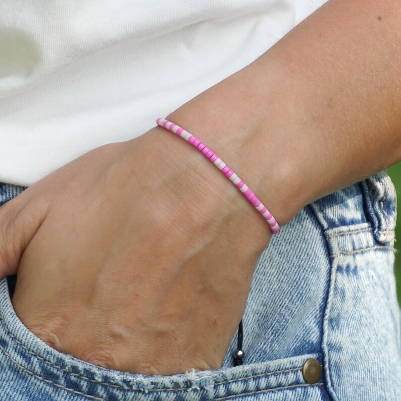 May include: A pink and white beaded bracelet on a person's wrist. The bracelet is made of small, round beads that are strung together on a thin cord.