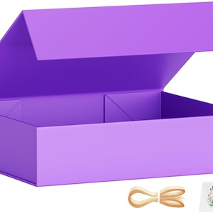 Op de afbeelding: Een helderpaarse geschenkdoos met een magnetische sluiting, gedeeltelijk open. Een beige lint en een kaart met een bloemenkrans en de tekst "Best Wishes" zijn inbegrepen. De doos is ontworpen om cadeau te geven.