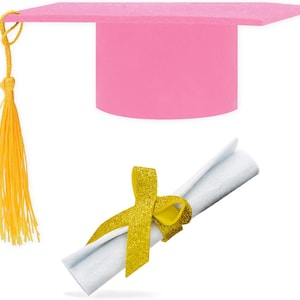Puede incluir: Un birrete rosa con una borla amarilla y un diploma enrollado atado con una cinta dorada con purpurina. El birrete tiene una parte superior cuadrada y una base cilíndrica. El diploma es blanco.