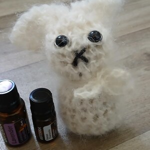 Può includere: Un coniglietto di lana bianco con occhi neri e naso nero. Due piccole bottiglie di vetro marrone con etichette nere sono davanti al coniglietto. Una bottiglia dice "Lavender" sull'etichetta.