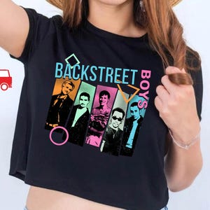 Puede incluir: Top corto negro con el texto "BACKSTREET BOYS" en verde azulado y naranja, y un gr&aacute;fico de los miembros de la banda. La camiseta est&aacute; hecha de material de lona negra.
