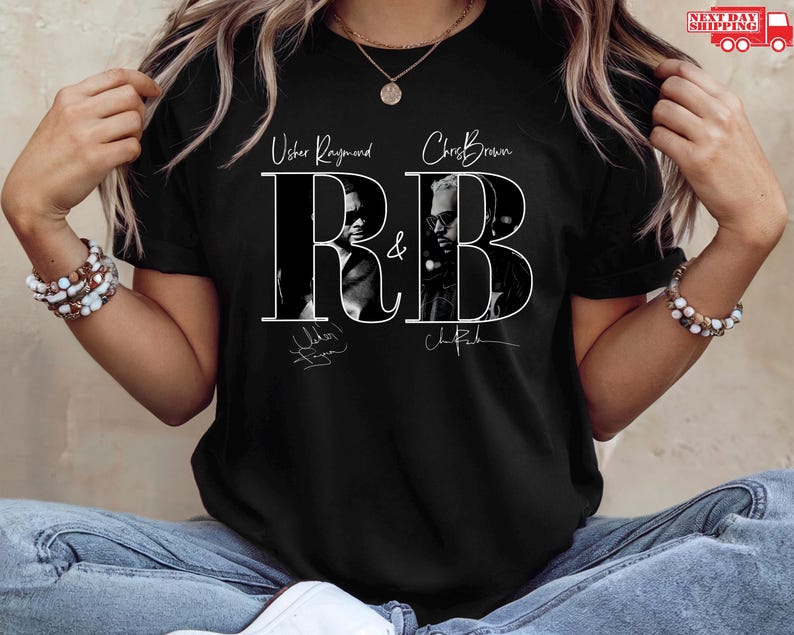May include: Black t-shirt featuring the text "R&B" with images of Usher Raymond and Chris Brown. The design includes their names and signatures in white. The shirt is worn by a person.