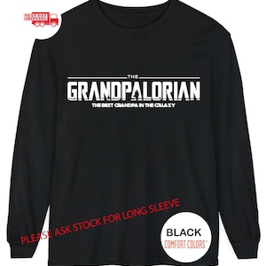 May include: Black long-sleeve t-shirt with white text that reads "THE GRANDPALORIAN THE BEST GRANDPA IN THE GALAXY". The text is in a bold, blocky font. The shirt also has the text "PLEASE ASK STOCK FOR LONG SLEEVE" and "BLACK COMFORT COLORS" in white.