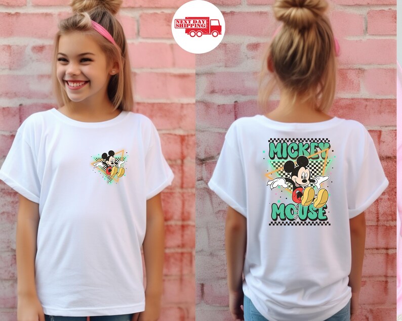 Puede incluir: Camiseta blanca con dise&ntilde;o de Mickey Mouse. La parte delantera tiene un peque&ntilde;o gr&aacute;fico de Mickey, mientras que la parte trasera muestra un dise&ntilde;o m&aacute;s grande con "Mickey Mouse" en letras verdes y negras. La camiseta tiene mangas cortas.