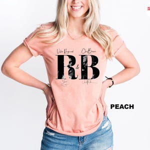 May include: Peach-colored t-shirt featuring the text "R&B" in large black letters with images of Usher Raymond and Chris Brown. The shirt also includes the names of the artists and their signatures. The word "PEACH" is printed in black.