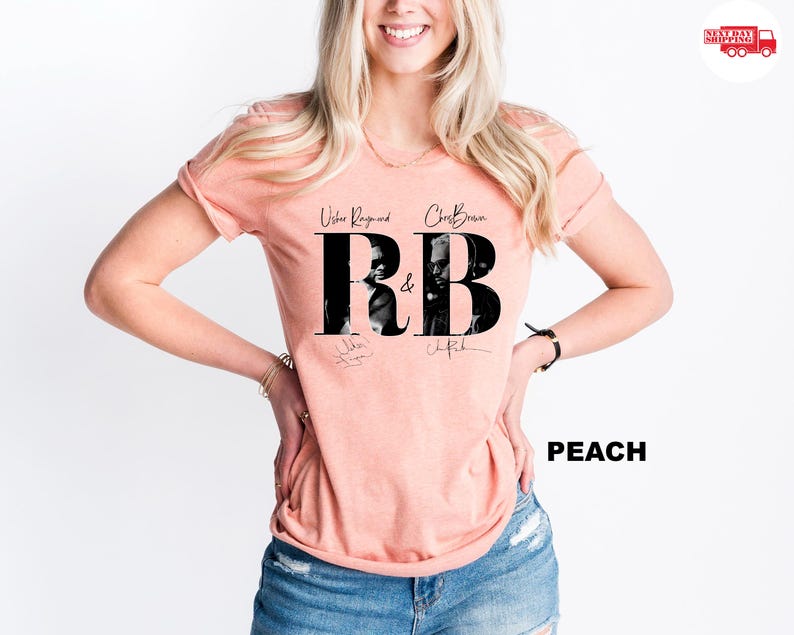 May include: Peach-colored t-shirt featuring the text "R&B" in large black letters with images of Usher Raymond and Chris Brown. The shirt also includes the names of the artists and their signatures. The word "PEACH" is printed in black.