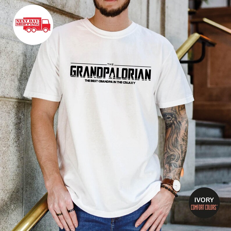 May include: White t-shirt with a black graphic that says "The Grandpalorian The Best Grandpa in the Galaxy".