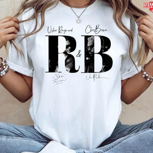 May include: White t-shirt featuring the text "Usher Raymond & Chris Brown R&B" in black, with black and white images of the artists within the letters. The shirt also includes the artists' signatures.