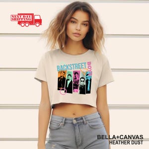 Puede incluir: Un crop top color crema con el texto "BACKSTREET BOYS" en turquesa y rosa, con im&aacute;genes de los miembros de la banda. La camiseta est&aacute; hecha de material Bella+Canvas Heather Dust.