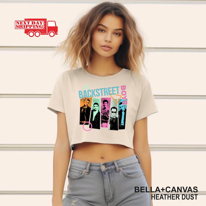 Puede incluir: Un crop top color crema con el texto "BACKSTREET BOYS" en turquesa y rosa, con im&aacute;genes de los miembros de la banda. La camiseta est&aacute; hecha de material Bella+Canvas Heather Dust.