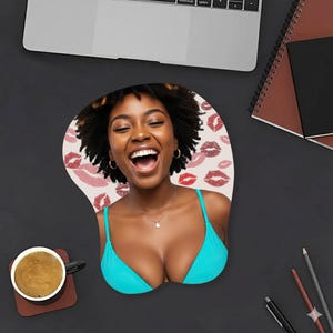 May include: A custom-shaped mousepad featuring a smiling person in a turquoise bikini top. The mousepad has a beige background with red and pink lipstick kiss marks. A cup of coffee and a laptop are also visible.