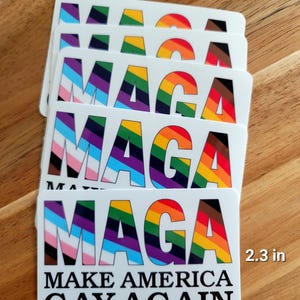 May include: A stack of white stickers with the text "MAGA" in rainbow colors and the words "MAKE AMERICA GAY AGAIN" in black. Each sticker measures 3.5 inches by 2.3 inches.