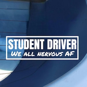 May include: White rectangular sticker with the text "STUDENT DRIVER" in a bold, sans-serif font, with the words "WE ALL NERVOUS AF" below. The sticker is on a car window, with a blue background.
