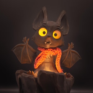 May include: A whimsical bat-shaped lamp with large, glowing yellow eyes and a knitted orange scarf. The bat is perched on a detailed, carved wooden base, resembling a tree stump. The lamp emits a warm, inviting glow, perfect for a child's room or a Halloween decoration.