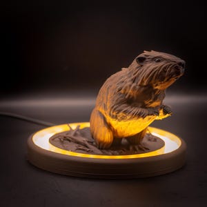 May include: A brown beaver figurine with a textured fur design, illuminated by a warm, yellow light. The beaver is perched on a circular base with a glowing ring, creating a soft, ambient glow. The base is approximately 15 cm in diameter.
