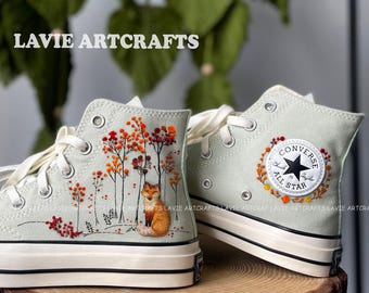 May include: A pair of light green high-top sneakers with embroidered designs. One shoe features a fox and autumn trees, the other a Converse All Star patch with floral accents. The text "LAVIE ARTCRAFTS" is visible.