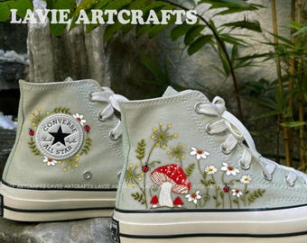 May include: A pair of light green high-top Converse sneakers with embroidered floral designs, including daisies, mushrooms, and ladybugs. The left shoe has the Converse All Star logo embroidered on the side. The text "LAVIE ARTCRAFTS" is visible at the top of the image.
