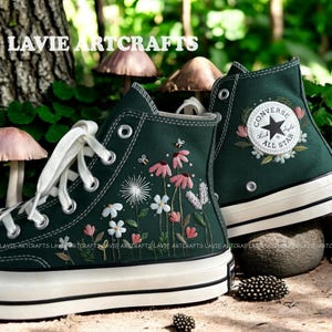 May include: Dark green high-top sneakers with white laces and soles. The sneakers feature embroidered floral designs in pink, white, and yellow, with a Converse All Star patch on the side. The text "LAVIE ARTCRAFTS" is visible.