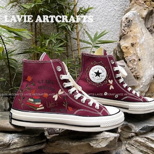 May include: Burgundy high-top Converse sneakers with a white sole and a white star logo. The shoes are hand-painted with a floral design, a stack of books, and the text "Stars Hollow Luke's Est 1779".