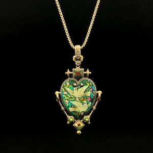 May include: Gold-coloured pendant necklace with a heart-shaped pendant. The pendant has a green enamel background with two white doves and floral accents. The necklace has a delicate chain and is set against a black background.