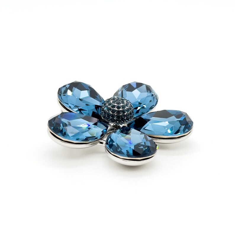 May include: A silver flower brooch with five blue crystal petals and a smaller blue crystal center.