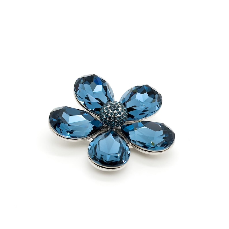 May include: A silver flower brooch with five blue crystal petals and a center crystal cluster.