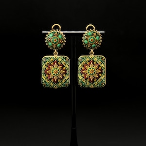 May include: A pair of gold-tone drop earrings featuring a circular top stud and a larger rectangular pendant. Both pieces are decorated with intricate enamel patterns in shades of green, red, and yellow, showcasing a symmetrical floral motif.