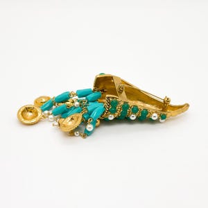 May include: A gold tone brooch with a turquoise and green stone design. The brooch is shaped like a horn and has a dangling chain with turquoise and pearl beads.