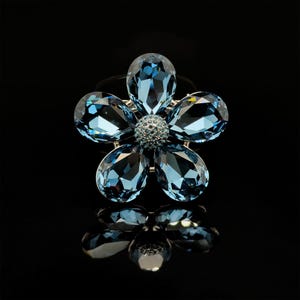 May include: A blue crystal flower brooch with a silver setting. The flower has five petals and a center stone.