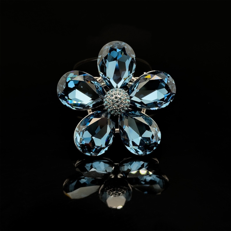 May include: A blue crystal flower brooch with a silver setting. The flower has five petals and a center stone.
