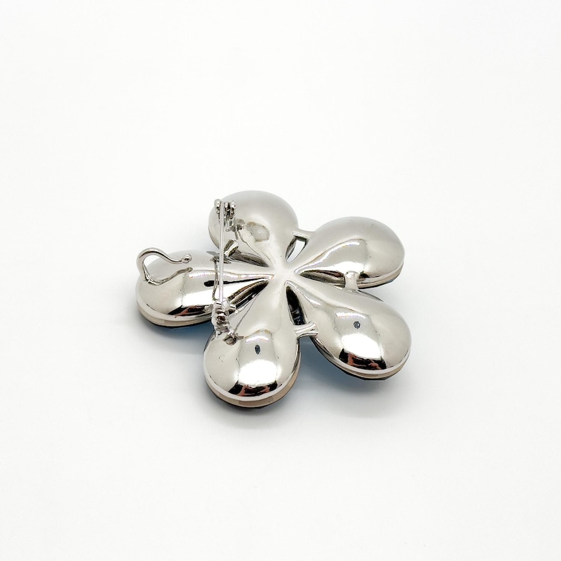 May include: Silver tone flower brooch with blue and white rhinestones. The brooch has a pin back.