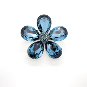 May include: A blue crystal flower brooch with a smaller crystal center.