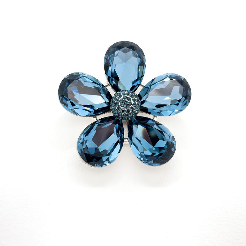 May include: A blue crystal flower brooch with a smaller crystal center.