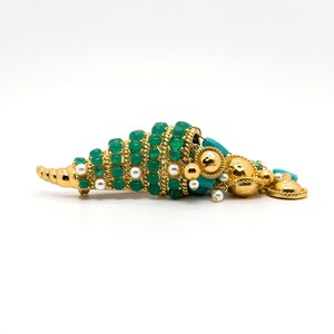 May include: A gold tone brooch with a turquoise and green shell design. The shell is decorated with white pearls and gold beads.