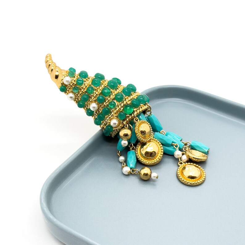 May include: A gold and green statement earring with a long, beaded tassel. The earring features a cone-shaped design with green beads and gold accents. The tassel is made of turquoise and white beads, and it hangs down from the bottom of the cone.