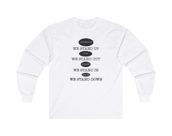 May include: White long-sleeve t-shirt with a graphic print of five black ovals with the text "We stand up", "We stand out", "We stand in", and "We stand down" in white text.