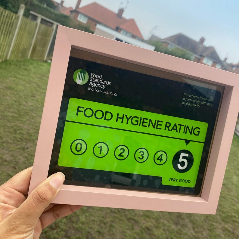 May include: A framed certificate with a green background and white text. The text reads "Food Hygiene Rating" and shows a rating of 5 out of 5, indicating "Very Good".